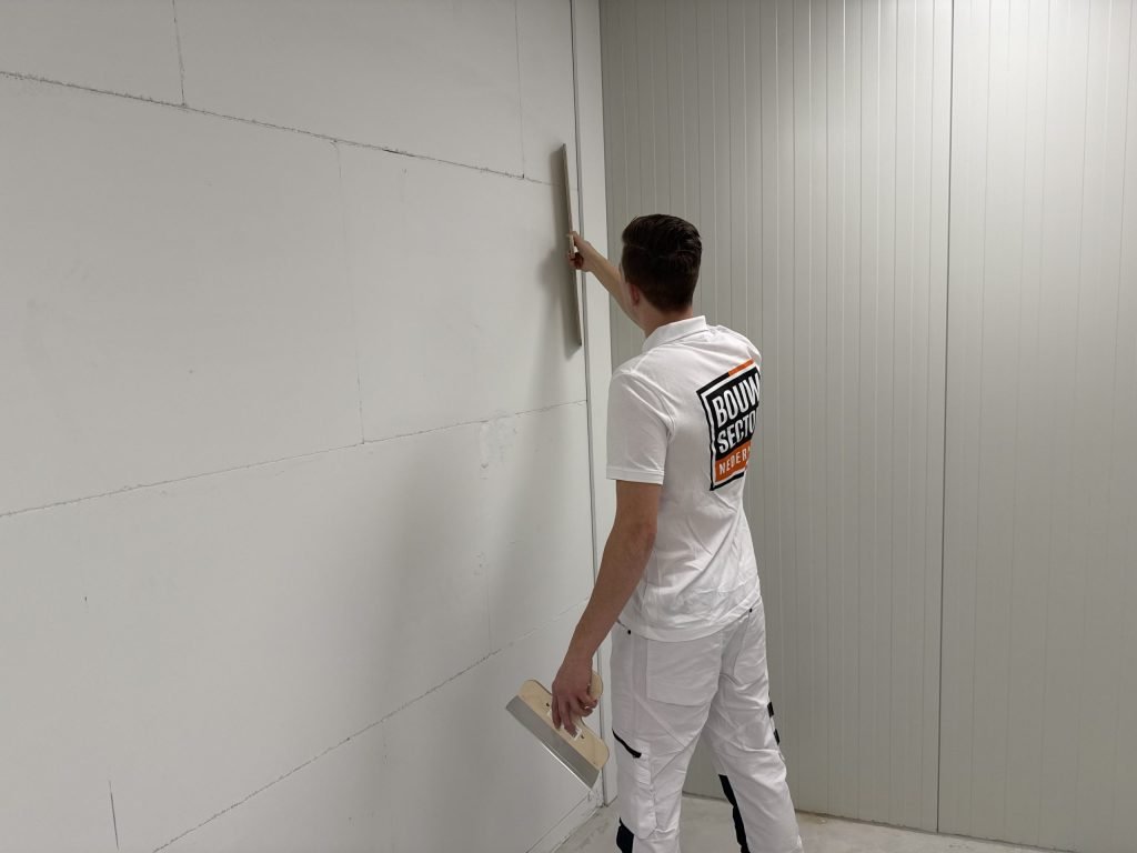 Stukadoor werkt een wand bij de hoek af met een lange spaan en houdt een plakspaan in zijn andere hand