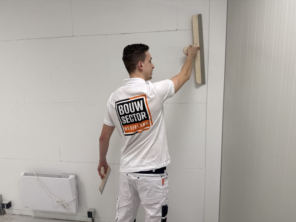Stukadoor van Bouwsector Nederland zet een wand glad naast een kachel