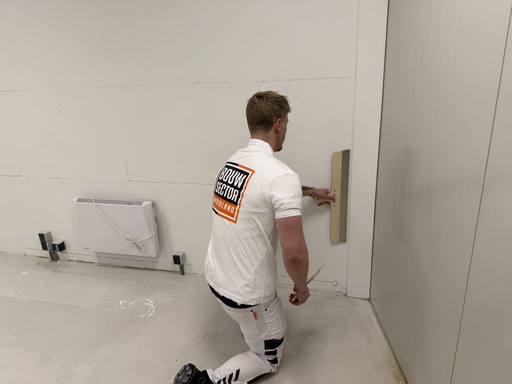 Stukadoor zit op zijn knie en trekt het onderste deel van een wand vlak met een spaan