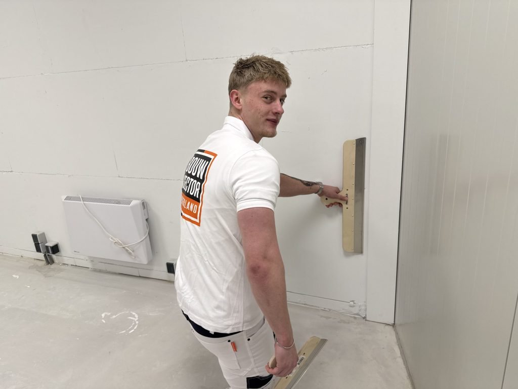 Stukadoor kijkt om terwijl hij een wand vlak zet met een lange spaan